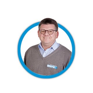 Ein lächelnder Mann mit Brille trägt einen grauen Pullover und ein kariertes Hemd, umrahmt von einem blauen Kreis.