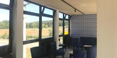Der Innenraum zeigt eine gemütliche Sitzecke mit blauen Polstermöbeln und Blick auf eine grüne Landschaft durch große Fenster.
