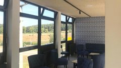 Der Innenraum zeigt eine gemütliche Sitzecke mit blauen Polstermöbeln und Blick auf eine grüne Landschaft durch große Fenster.