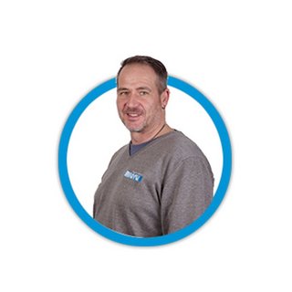 Ein Mann mit einem freundlichen Lächeln trägt ein graues Oberteil und steht vor einem weißen Hintergrund in einem blauen Kreis.