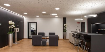 Ein modernes Wartezimmer mit eleganten Möbeln, einer Bar und stilvollen Orchideen in silbernen Vasen.