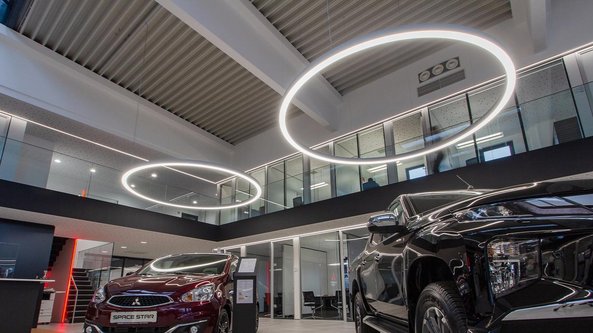 Ein modernes Autohaus mit zwei Fahrzeugen, einem roten und einem schwarzen Auto, unter stilvollen, runden Deckenleuchten.