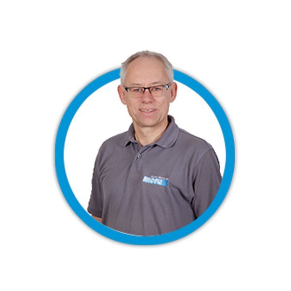 Ein lächelnder Mann mit Brille trägt ein graues Polohemd und steht vor einem weißen Hintergrund in einem runden Rahmen.