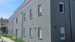 Die Fassade eines neuen Wohnhauses, das mit hellen Fensterläden und einem gepflegten Gartenbereich gestaltet ist.