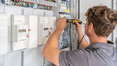 Ein Techniker überprüft mit einem Messgerät die elektrischen Zähler in einem modernen Verteilerkasten.