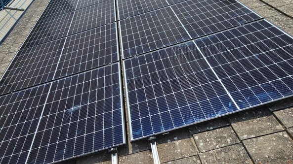 Eine Gruppe von Solarpanelen liegt auf einem Dach, die Sonnenstrahlen reflektieren sich auf den glänzenden Oberflächen.