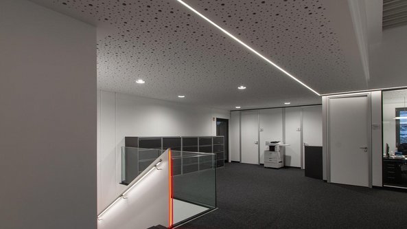 Ein modernes Büro mit einem eleganten Treppenaufgang, der von einer Glasbrüstung und einer roten LED-Leuchte beleuchtet wird.