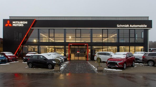 Das moderne Mitsubishi-Autohaus zeigt eine Vielzahl von Fahrzeugen, die auf dem Parkplatz mit leichtem Schnee bedeckt sind.