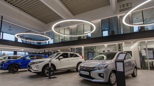 Ein modernes Autohaus mit mehreren Fahrzeugen, darunter ein blauer SUV und ein silberner Kleinwagen, in einem hellen Raum.