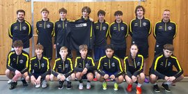 Eine Gruppe von jungen Sportlern in schwarzen Trainingsanzügen mit gelben Akzenten posiert lächelnd in einer Sporthalle.