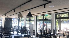 Der Innenraum eines Restaurants, in dem die Stühle auf den Tischen stehen, während draußen Bäume und Spielgeräte sichtbar sind.