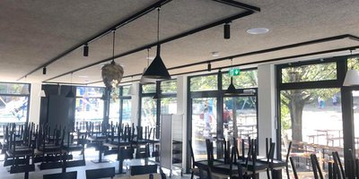 Der Innenraum eines Restaurants, in dem die Stühle auf den Tischen stehen, während draußen Bäume und Spielgeräte sichtbar sind.
