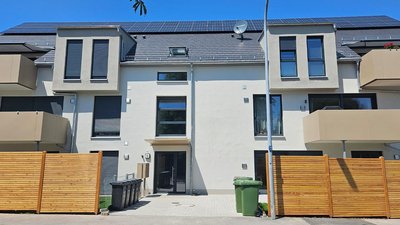 Ein modernes Wohngebäude mit Solarzellen auf dem Dach und großen Fenstern, umgeben von einem Holzzaun.