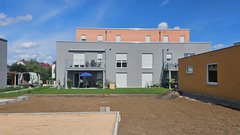 Zwei moderne Wohngebäude stehen nebeneinander, umgeben von einem gepflegten Garten und einem blauen Himmel mit wenigen Wolken.