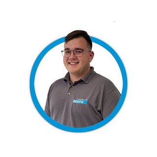 Ein junger Mann mit Brille lächelt freundlich in einem grauen Poloshirt mit einem blauen Logo auf der linken Brust.