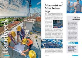 Auf einer Baustelle arbeiten mehrere Personen mit Helmen an einem Plan, während im Hintergrund ein Kran und das Meer sichtbar sind.