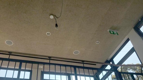 Ein Blick auf die Decke eines hellen Raumes, der mit Lautsprechern und einer Notausgangsanzeige ausgestattet ist.