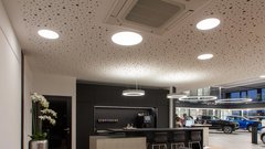 Ein modernes Autohaus mit eleganter Einrichtung, beleuchtet von runden Deckenleuchten und einem stilvollen Empfangstresen.