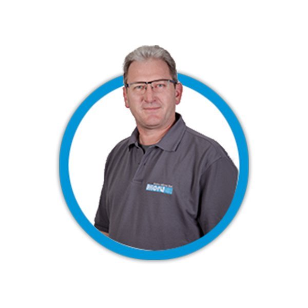 Ein Mann mit grauen Haaren trägt ein graues Polohemd und Brille, lächelt freundlich in einem runden Rahmen.