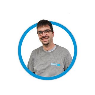 Ein lächelnder Mann mit Brille trägt ein graues T-Shirt und steht vor einem weißen Hintergrund in einem runden Rahmen.