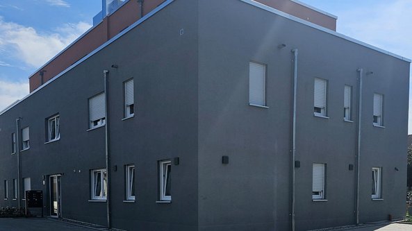 Ein modernes, graues Gebäude mit großen Fenstern und einem klaren, minimalistischen Design unter einem blauen Himmel.