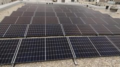 Eine große Fläche mit Solarpanelen auf einem Dach, die in einem gleichmäßigen Muster angeordnet sind und Sonnenlicht reflektieren.