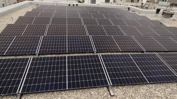 Eine große Fläche mit Solarpanelen auf einem Dach, die in einem gleichmäßigen Muster angeordnet sind und Sonnenlicht reflektieren.