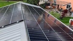 Auf dem Dach sind mehrere Solarpanels installiert, die in der Sonne glänzen und umgeben von einem grünen Garten sind.