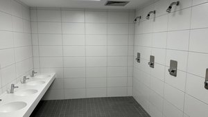 Ein modernes Badezimmer mit weißen Fliesen, das fünf Waschbecken und mehrere Duschköpfe an der Wand zeigt.