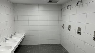 Ein modernes Badezimmer mit weißen Fliesen, das fünf Waschbecken und mehrere Duschköpfe an der Wand zeigt.