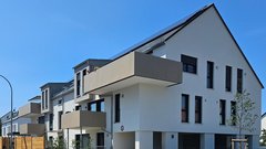 Moderne Wohngebäude mit hellen Fassaden und großen Fenstern, umgeben von einem klaren blauen Himmel.