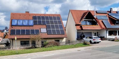 Zwei Häuser mit roten Dächern, beide mit Solarpanelen, stehen nebeneinander in einer ruhigen Wohngegend.