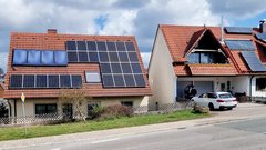 Zwei Häuser mit roten Dächern, beide mit Solarpanelen, stehen nebeneinander in einer ruhigen Wohngegend.