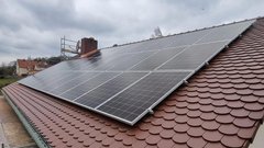 Auf einem Dach sind mehrere Solarpanels installiert, die auf einem braunen Schindeldach montiert sind, unter einem bewölkten Himmel.