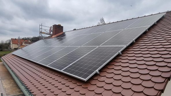Auf einem Dach sind mehrere Solarpanels installiert, die auf einem braunen Schindeldach montiert sind, unter einem bewölkten Himmel.