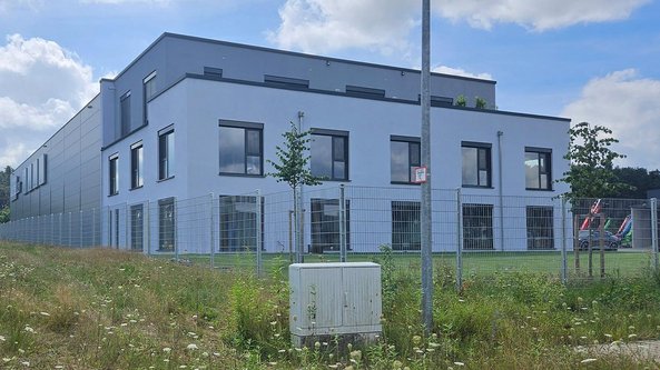 Ein modernes, zweigeschossiges Gebäude mit großen Fenstern und einem gepflegten Gartenbereich im Vordergrund.