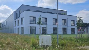 Ein modernes, zweigeschossiges Gebäude mit großen Fenstern und einem gepflegten Gartenbereich im Vordergrund.