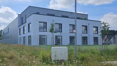 Ein modernes, zweigeschossiges Gebäude mit großen Fenstern und einem gepflegten Gartenbereich im Vordergrund.
