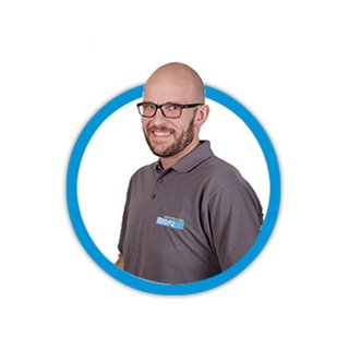 Ein lächelnder Mann mit Brille trägt ein graues Poloshirt und steht vor einem weißen Hintergrund in einem runden Rahmen.