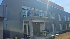 Ein modernes, graues Gebäude mit einem Balkon, der mit bunten Blumen dekoriert ist, und einem gemütlichen Essbereich im Freien.