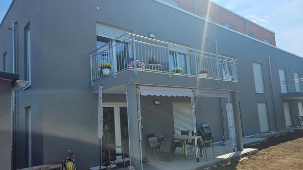 Ein modernes, graues Gebäude mit einem Balkon, der mit bunten Blumen dekoriert ist, und einem gemütlichen Essbereich im Freien.