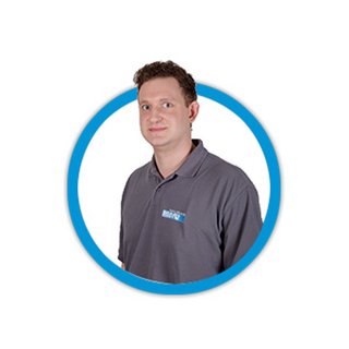 Ein Mann mit kurzen braunen Haaren trägt ein graues Polohemd und lächelt leicht in die Kamera.