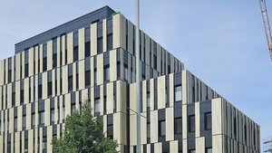 Ein modernes Gebäude mit einer einzigartigen Fassade aus schwarzen und hellen vertikalen Elementen, umgeben von einem blauen Himmel.
