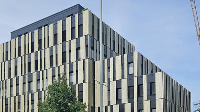 Ein modernes Gebäude mit einer einzigartigen Fassade aus schwarzen und hellen vertikalen Elementen, umgeben von einem blauen Himmel.