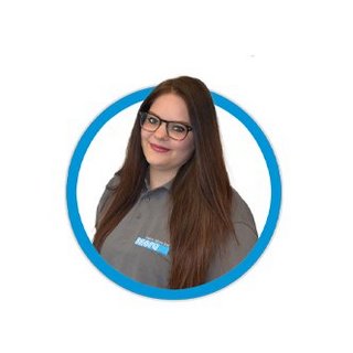 Eine lächelnde Frau mit langen, braunen Haaren trägt ein graues Hemd und eine Brille, umgeben von einem blauen Kreis.