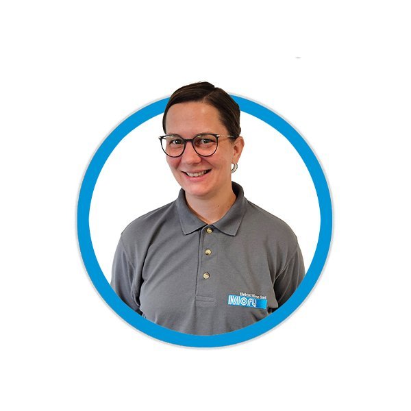 Eine lächelnde Person mit Brille trägt ein graues Poloshirt und steht vor einem weißen Hintergrund.
