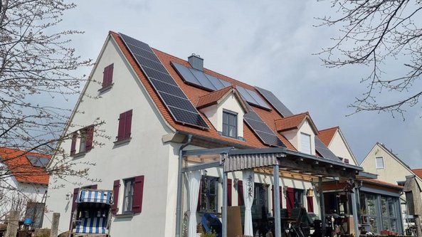 Ein modernes Haus mit roten Fensterläden und Solarpanelen auf dem Dach, umgeben von frischen, blühenden Bäumen.