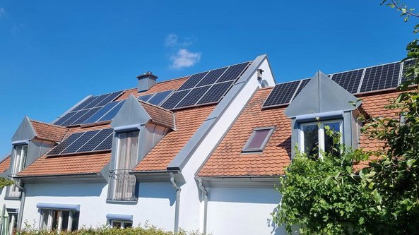 Ein modernes Haus mit einem schrägen Dach, das mit mehreren Solarpanelen bedeckt ist, unter einem strahlend blauen Himmel.