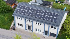 Ein modernes Wohnhaus mit Solarpanelen auf dem Dach, umgeben von grünem Gras und Bäumen, strahlt Nachhaltigkeit aus.