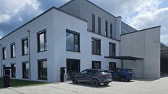 Ein modernes, zweigeschossiges Gebäude mit großen Fenstern und einem klaren, minimalistischen Design, umgeben von grünem Rasen.